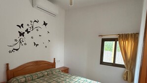 Ein Schlafzimmer mit Bett, Deckenventilator, Fenster mit Vorhängen und Wanddekoration.
