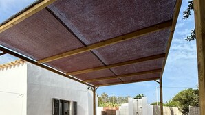 Eine überdachte Terrasse im Freien mit zwei Liegestühlen, einem Tisch und einer Grillgelegenheit.