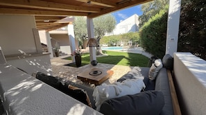 A covered outdoor seating area with a stone table, cushions, and a decorative lamp.