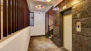 A hallway with a marble floor, a staircase with metal railings, and an elevator with a granite wall. - Treebo Three Street Inn (Bengaluru)