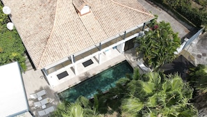 An aerial view of a building with a tiled roof, a swimming pool, and surrounding greenery.