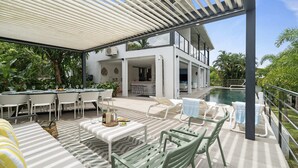 An outdoor patio with a pool, white furniture, and a covered seating area.