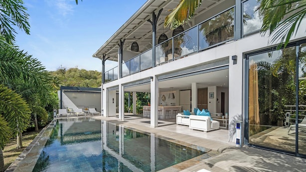 A modern house with a large swimming pool, a covered outdoor area, and a balcony with a view of the pool.