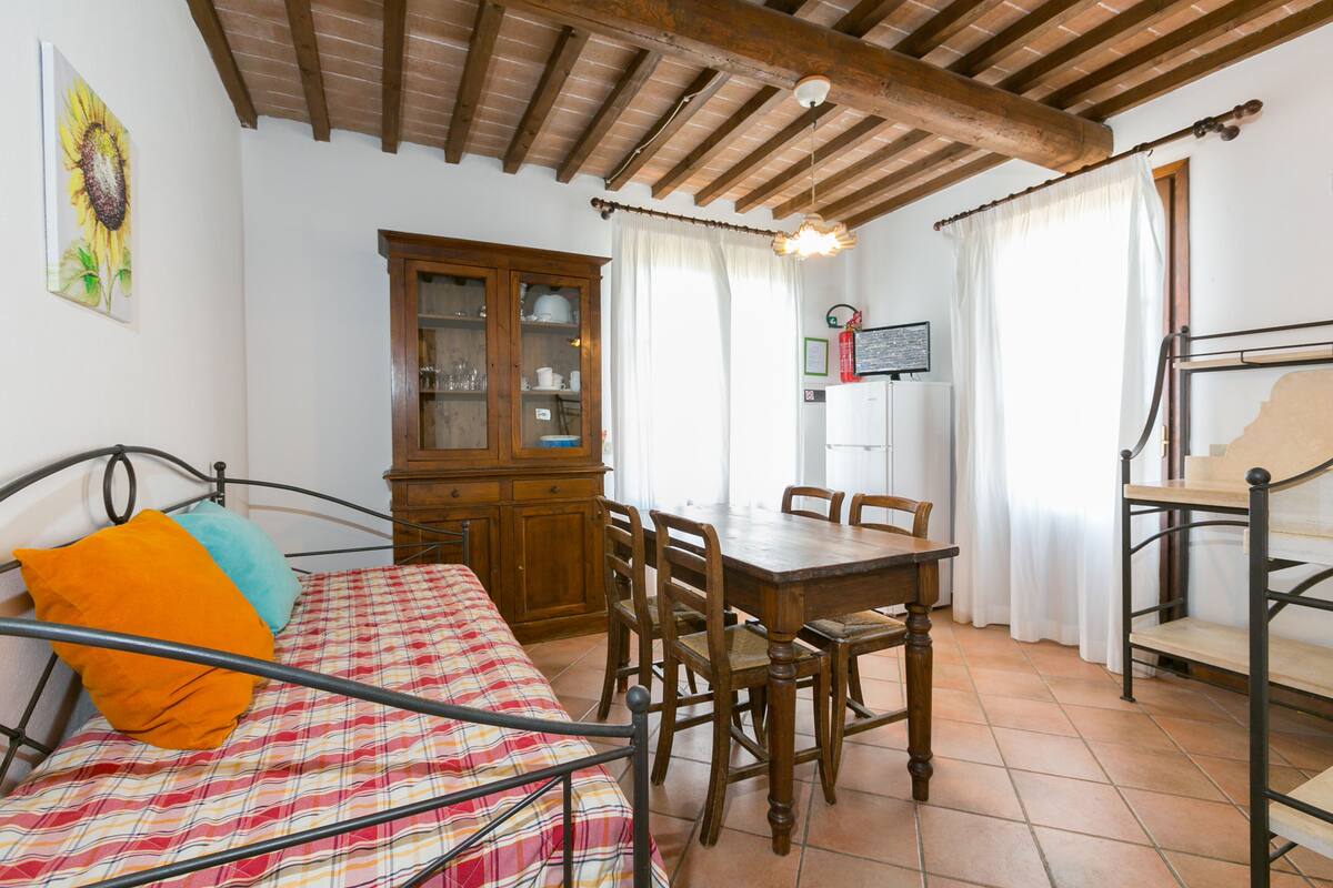 A bedroom with a bed, a wooden dining table with chairs, a cabinet, and a ceiling with exposed beams.
