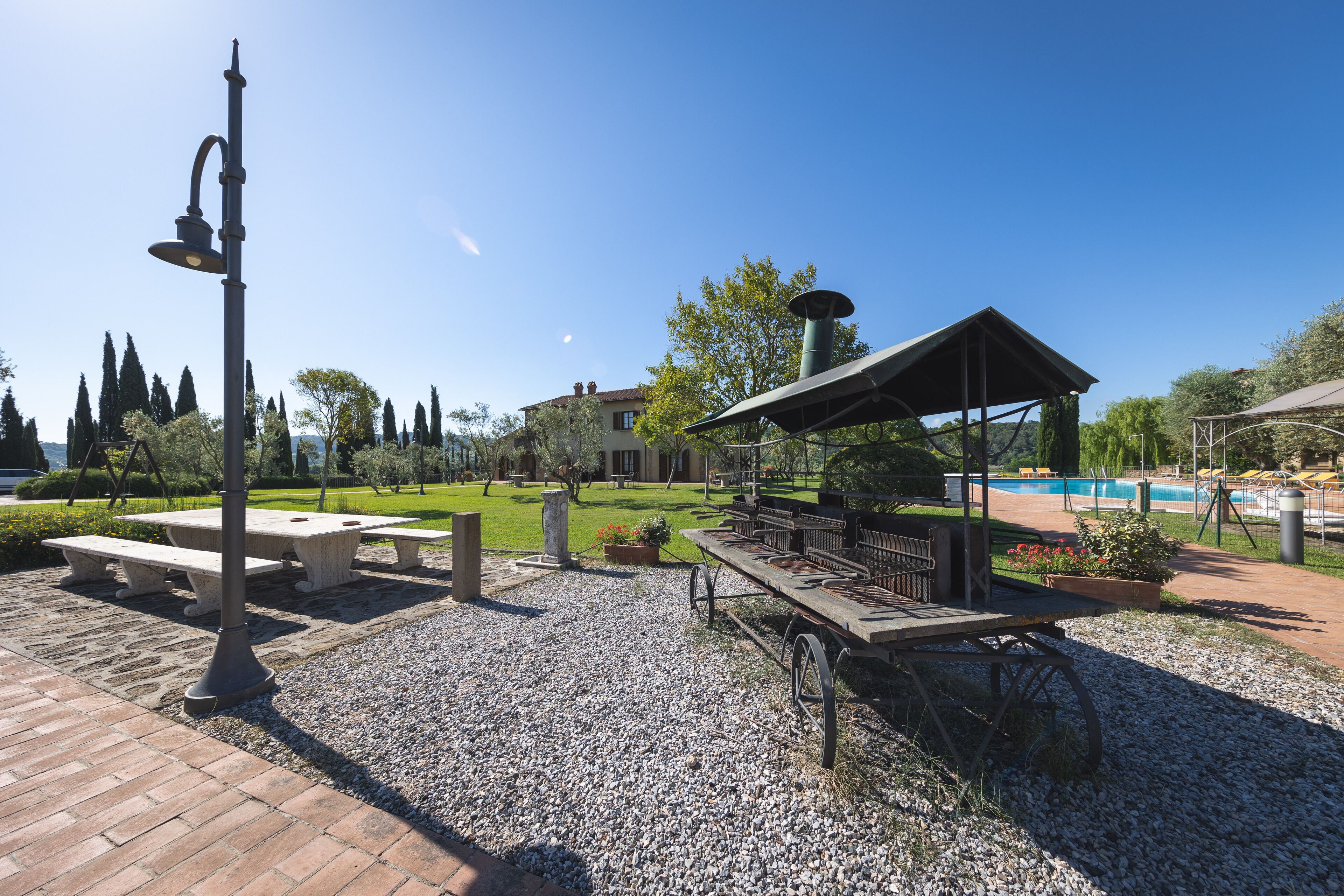 Un espace extérieur aménagé avec une terrasse, une table de pique-nique, une pergola et une piscine en arrière-plan.