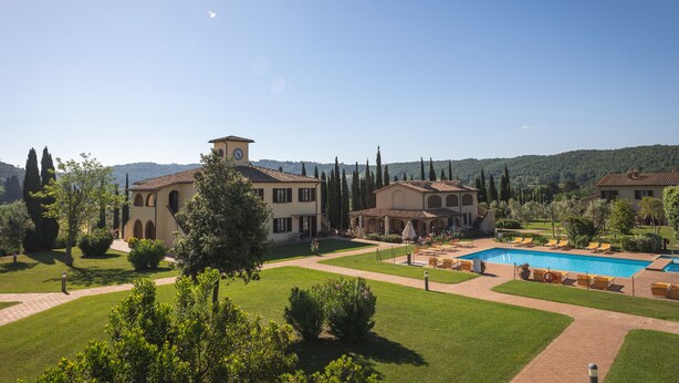 Una amplia villa con piscina, rodeada de un césped cuidado y árboles.