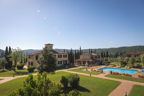 Una amplia villa con piscina, rodeada de un césped cuidado y árboles.