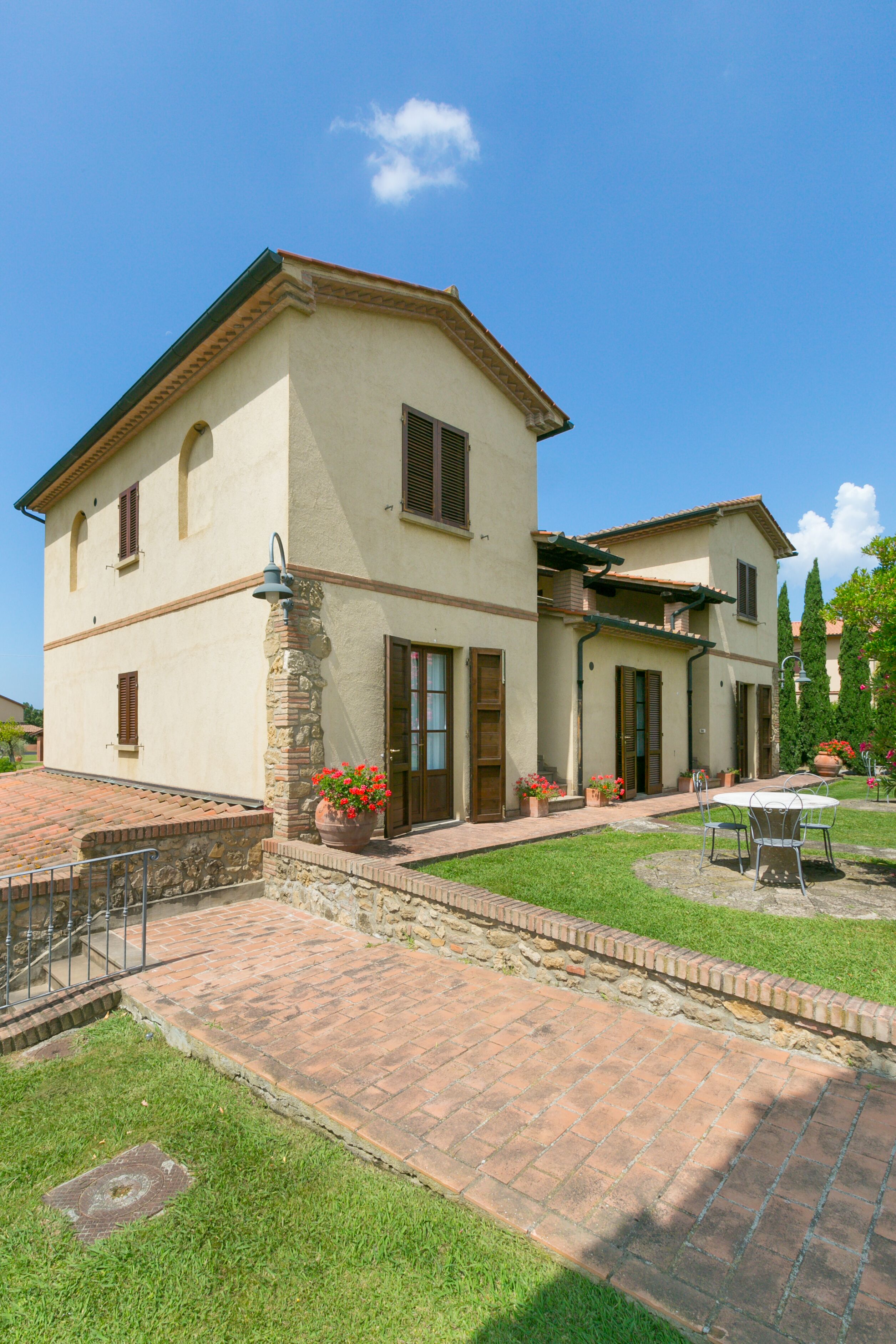 A two-story house with a patio area, stone pillars, and potted plants.