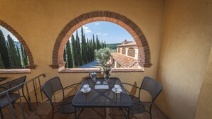Una terraza con mesa y sillas, vista a un pueblo a través de un arco, y un muro de ladrillo.