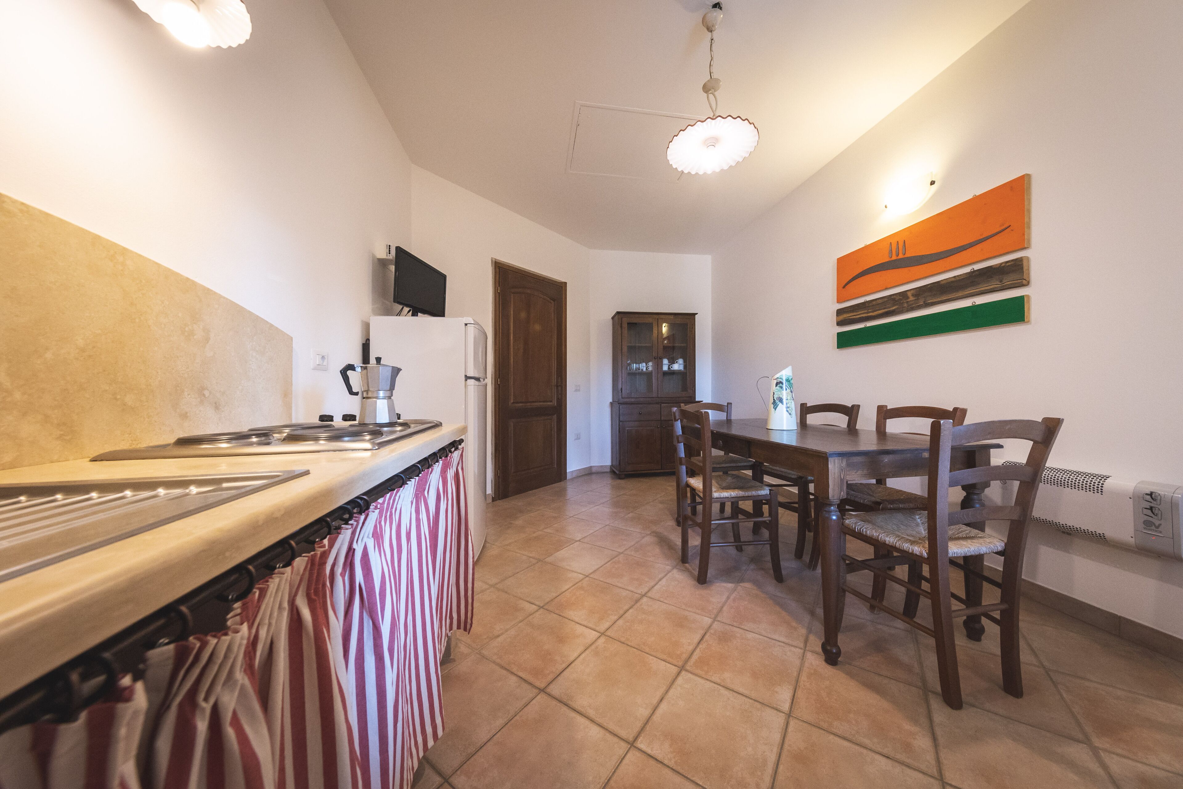 A kitchen with a stove, oven, and cabinets, a dining table with chairs, and a ceiling light.