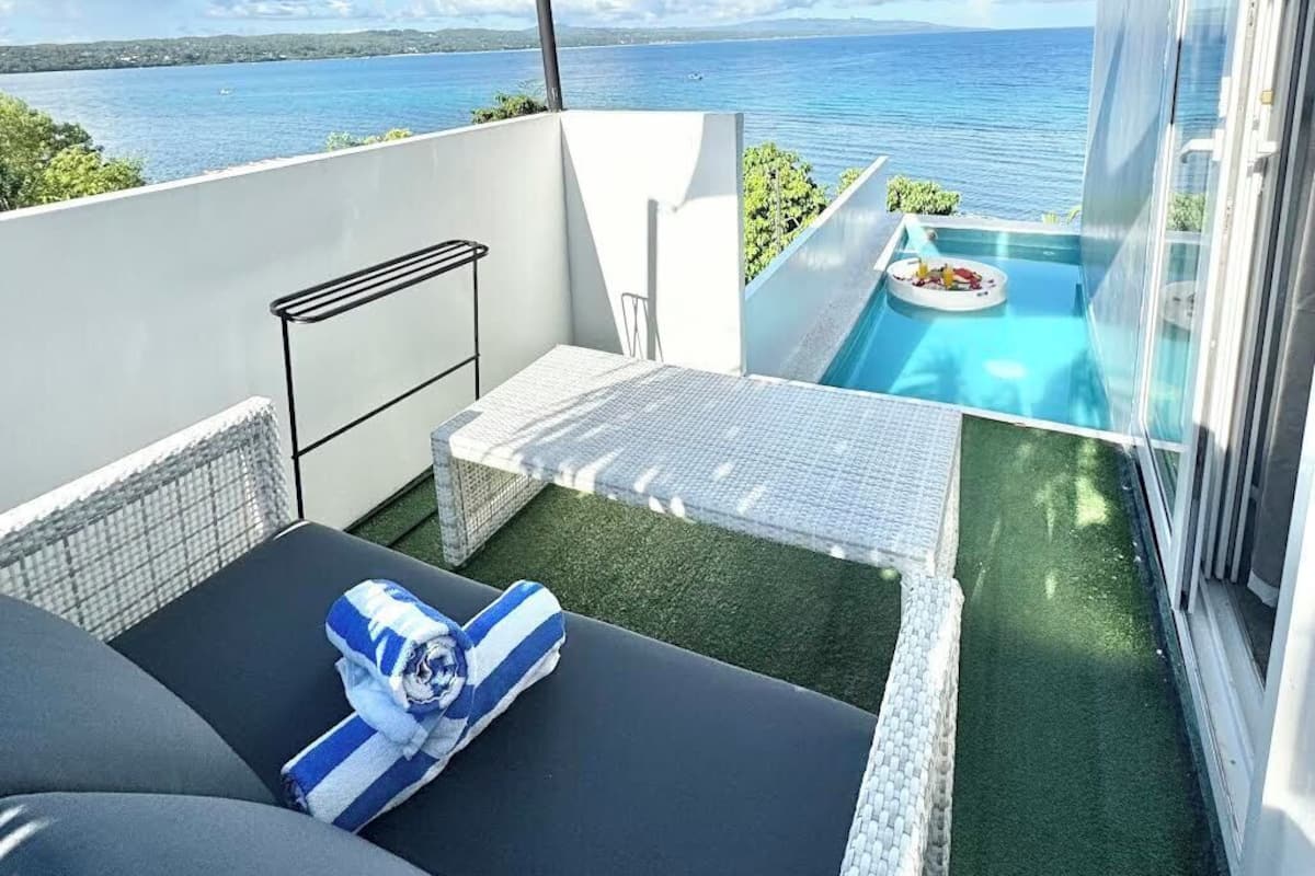 En balkong med utsikt över havet, en liten pool och en loungehörna med en soffa och ett bord.