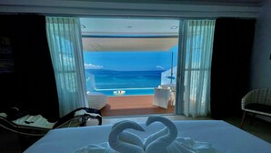 Une chambre avec un lit, une vue sur l’océan et un balcon équipé d’une table et de chaises.