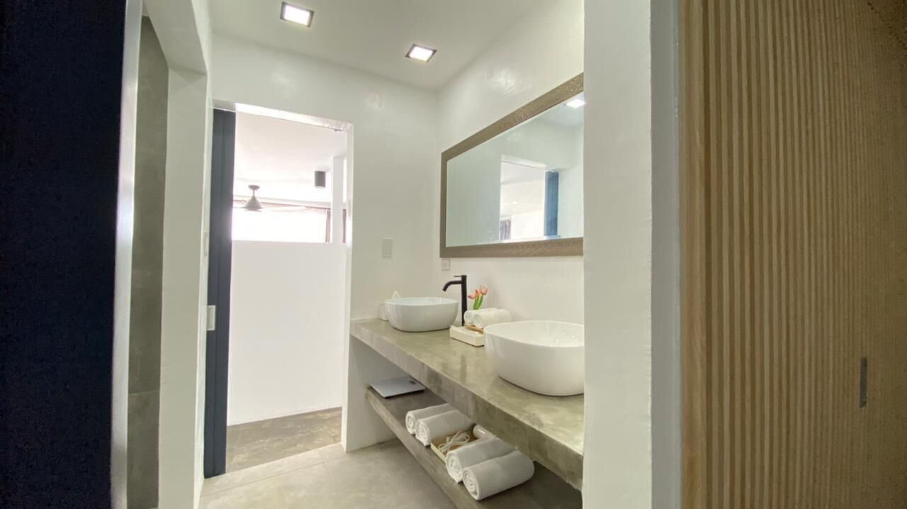 Un baño moderno con un espejo grande, un lavamanos blanco y un perchero para toallas.