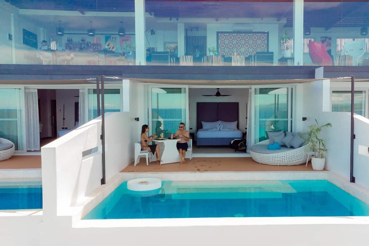 Ett modernt hotellrum i två våningar med balkong, pool och en matplats.