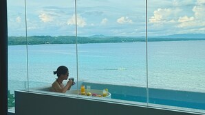 Une personne dans une baignoire, avec vue sur une étendue d’eau et sur une terre lointaine.