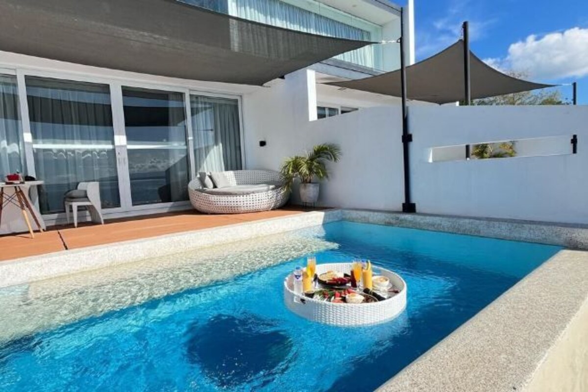 A swimming pool with a floating bar area, a covered seating area, and a modern building with large windows.