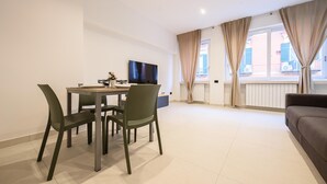 A modern living room with a dining area, a flat-screen TV, and large windows with curtains. - Via Niccolo Tommaseo 4 - Appartamento 1 (Naples)