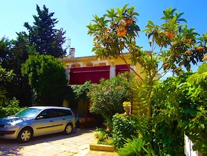 A residential area with a parked car, a building with red shutters, and lush greenery.