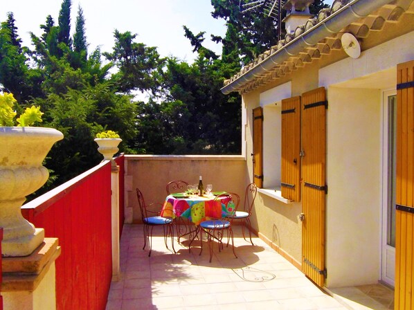 Une petite terrasse extérieure avec une table et des chaises, une plante en pot et une porte en bois.