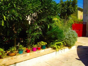 Un jardín con diferentes plantas en macetas y un portón rojo al fondo.