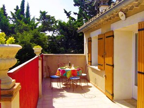Un pequeño patio al aire libre con una mesa, sillas, una planta en maceta y una puerta de madera.