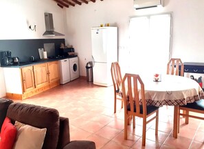 A compact kitchen with a washing machine, a refrigerator, and a dining area with a table and chairs.
