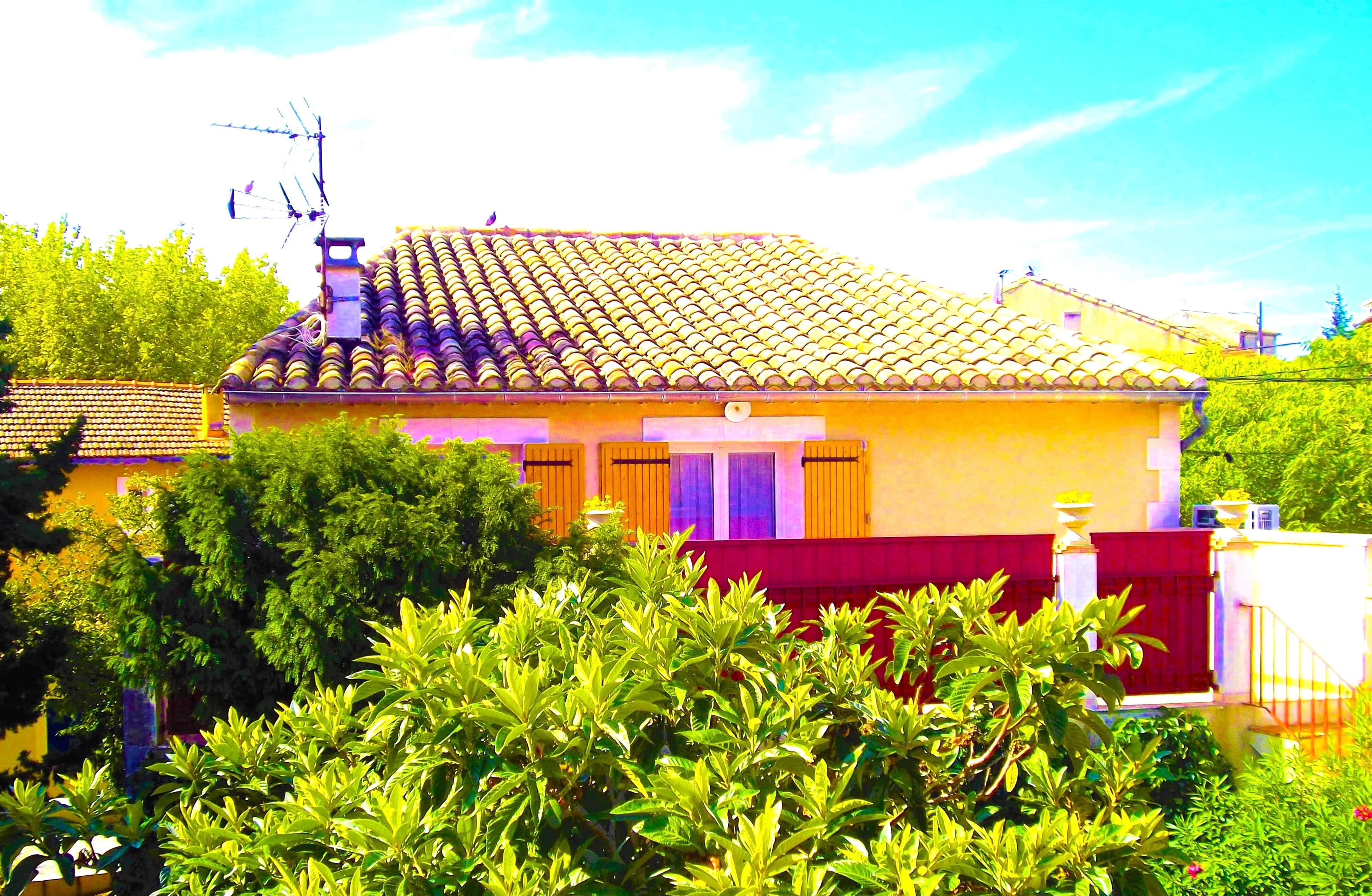 A residential building with a tiled roof, a red fence, and lush greenery in the foreground.