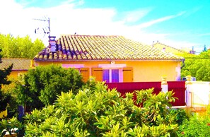 Un immeuble résidentiel avec un toit recouvert de tuiles, une clôture rouge et une végétation luxuriante au premier plan.