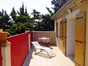 A small outdoor patio with a table and chairs, a red fence, and a wooden door.