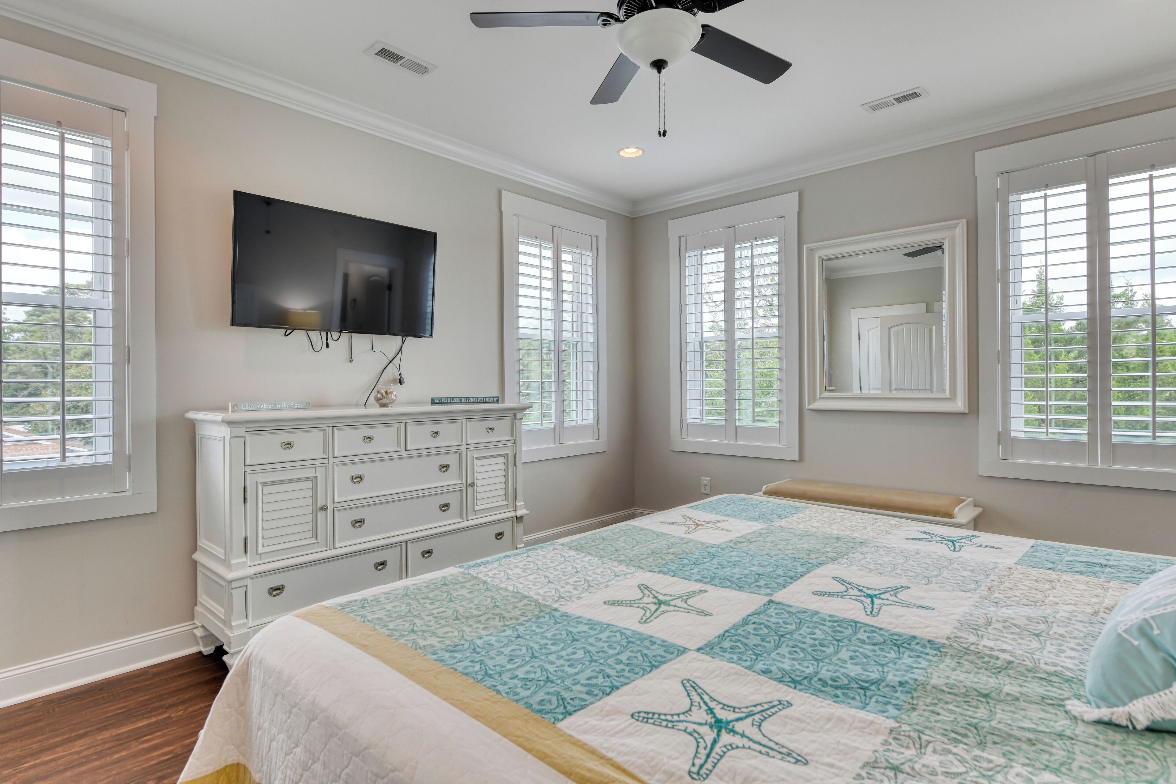 A bedroom with a bed, dresser, TV, and windows.