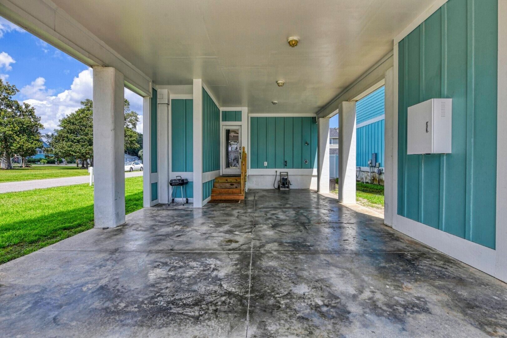 A covered outdoor area with teal walls and a concrete floor, leading to a door.
