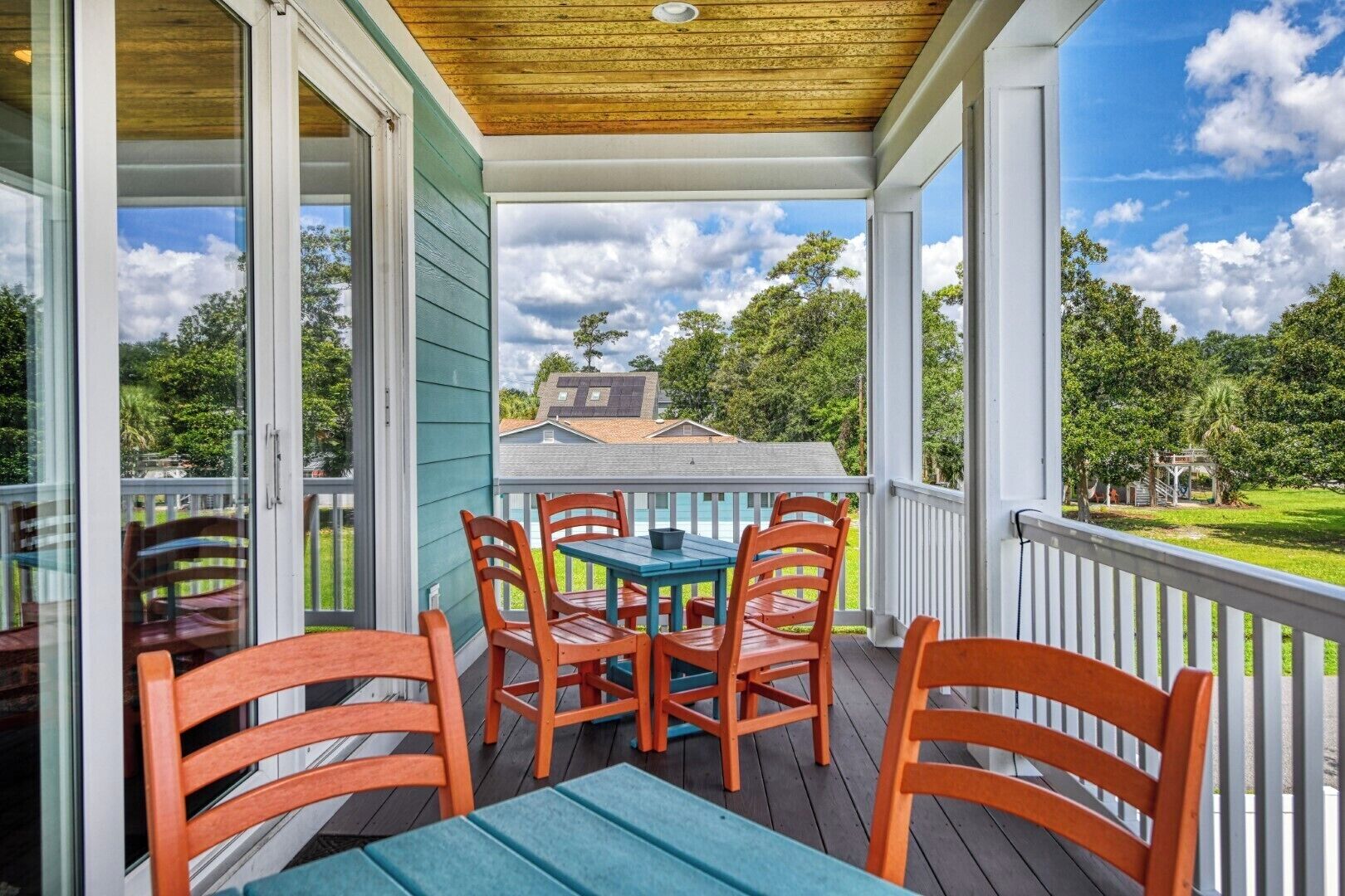 A covered outdoor area with a table and chairs, a view of a house and trees in the background.