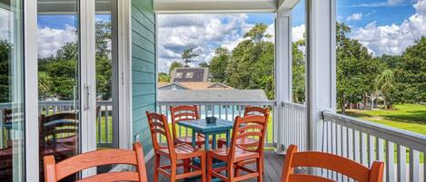 A covered outdoor area with a table and chairs, a view of a house and trees in the background.