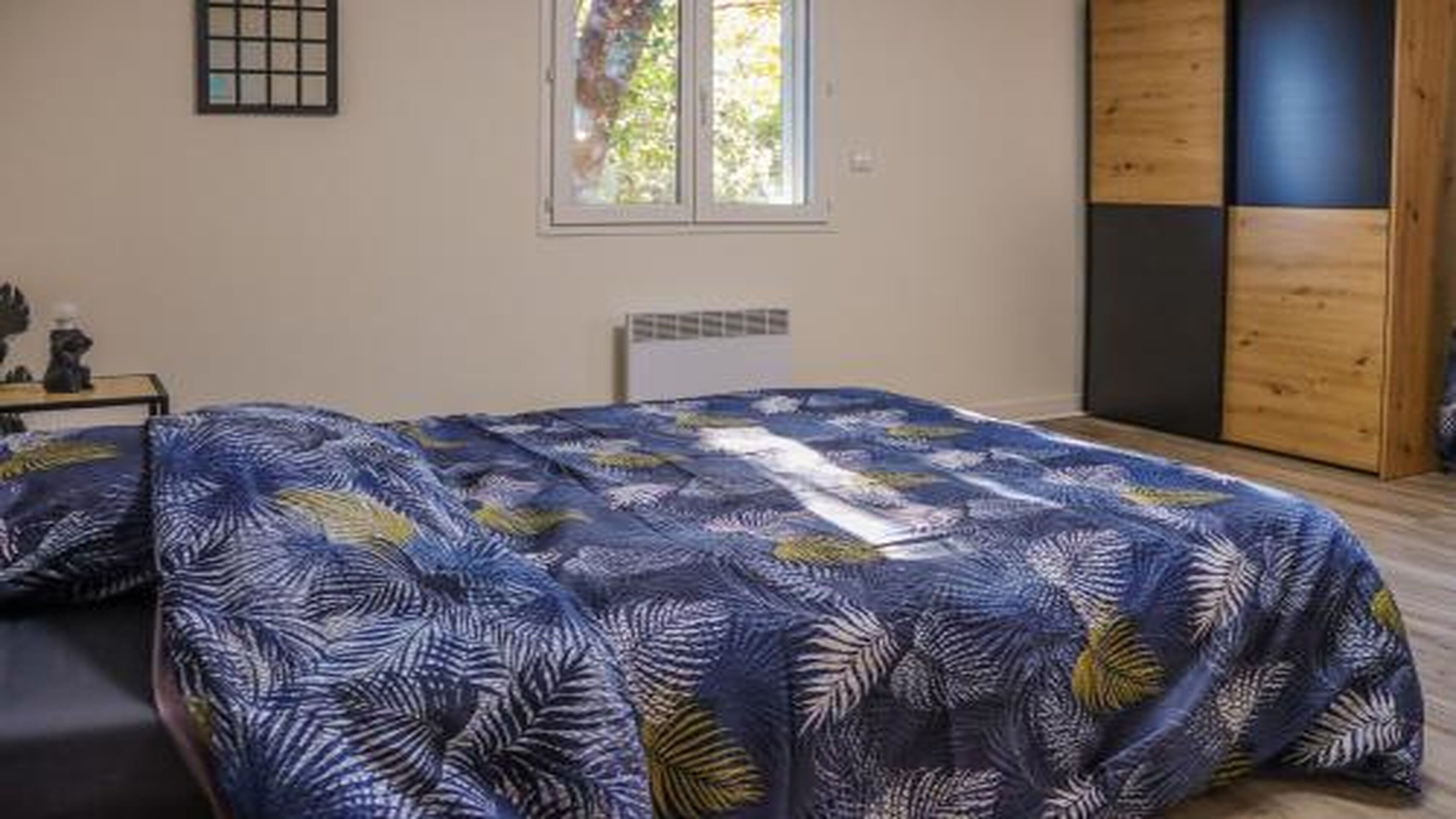 A bedroom with a large bed, a window, a radiator, and a wardrobe.