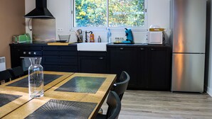A modern kitchen with a dining table, chairs, a refrigerator, and a window with a view of trees. - Duplex Le Philandra - 2-4 pers - jacuzzi  (Monteils)