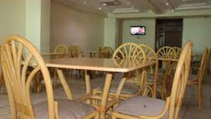 A dining area with wicker chairs and a table, a television on the wall, and a door in the background. - Roof Galaxy Hotel (Machakos)