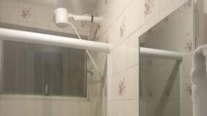 Zona de ducha con puerta de vidrio, una toalla blanca colgada en la pared y un cabezal de ducha en el techo.