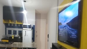 Una cocina moderna con microondas integrado, refrigerador y un televisor de pantalla plana grande montado en la pared. Hay tres taburetes de bar con asientos amarillos y un salpicadero de azulejos.