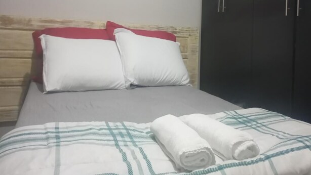 Una cama con almohadas blancas y rojas, un edredón a rayas y toallas enrolladas.