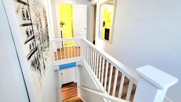 Een trap met witte leuningen en een houten handrail, leidend naar een kamer met een gele deur.