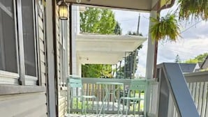 Een aantal donkerhouten traptreden die leiden naar een veranda met een leuning, een tafeltje en stoelen.