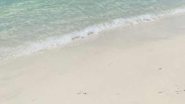 A beach with clear turquoise water, a boat in the distance, and a clear sky.