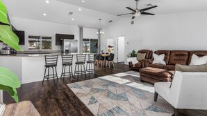 A modern kitchen with a central island, dark wooden flooring, and a dining area with bar stools.