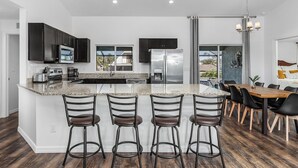 A modern kitchen with dark cabinets, a central island with bar stools, stainless steel appliances, and a dining area with a wooden table and chairs.