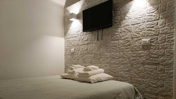 A bedroom with a stone wall, a flat-screen TV mounted above the bed, and neatly folded towels on the bed. - Mirosa mini loft for you. (Bari)