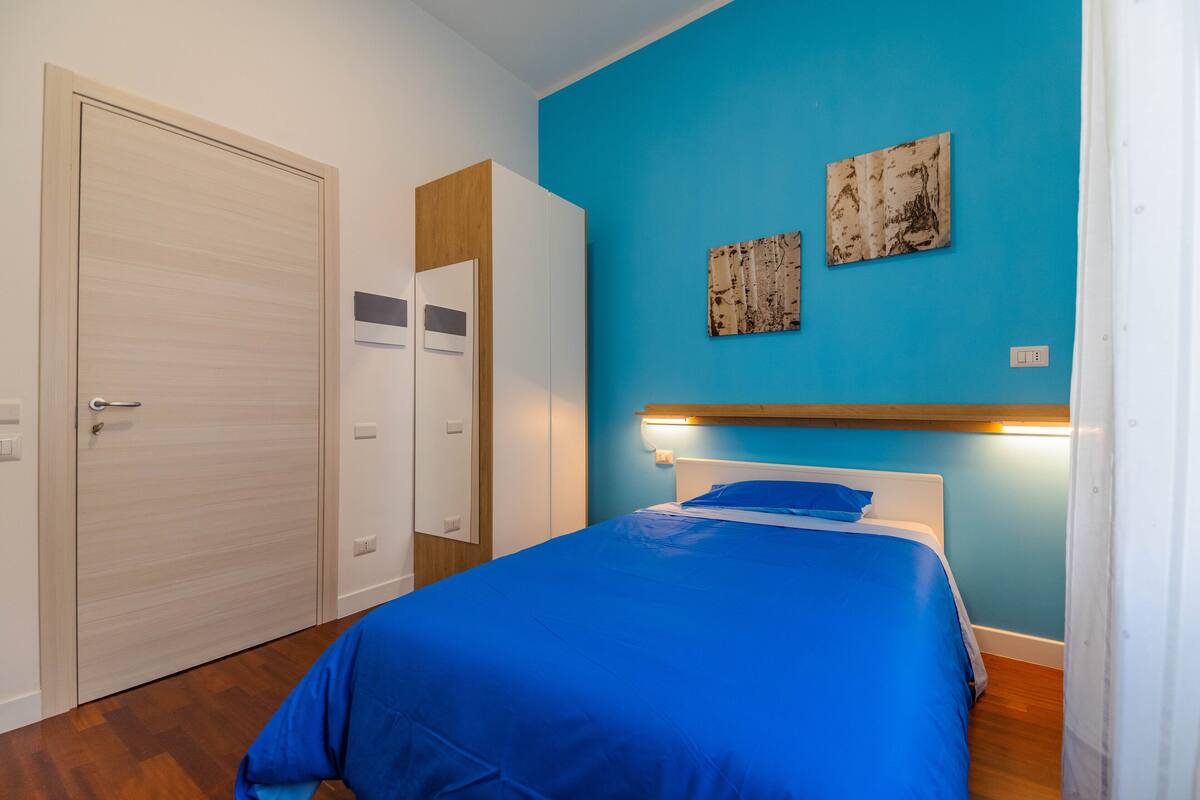 A bedroom with a blue bedspread, a wooden headboard, and two wall art pieces.