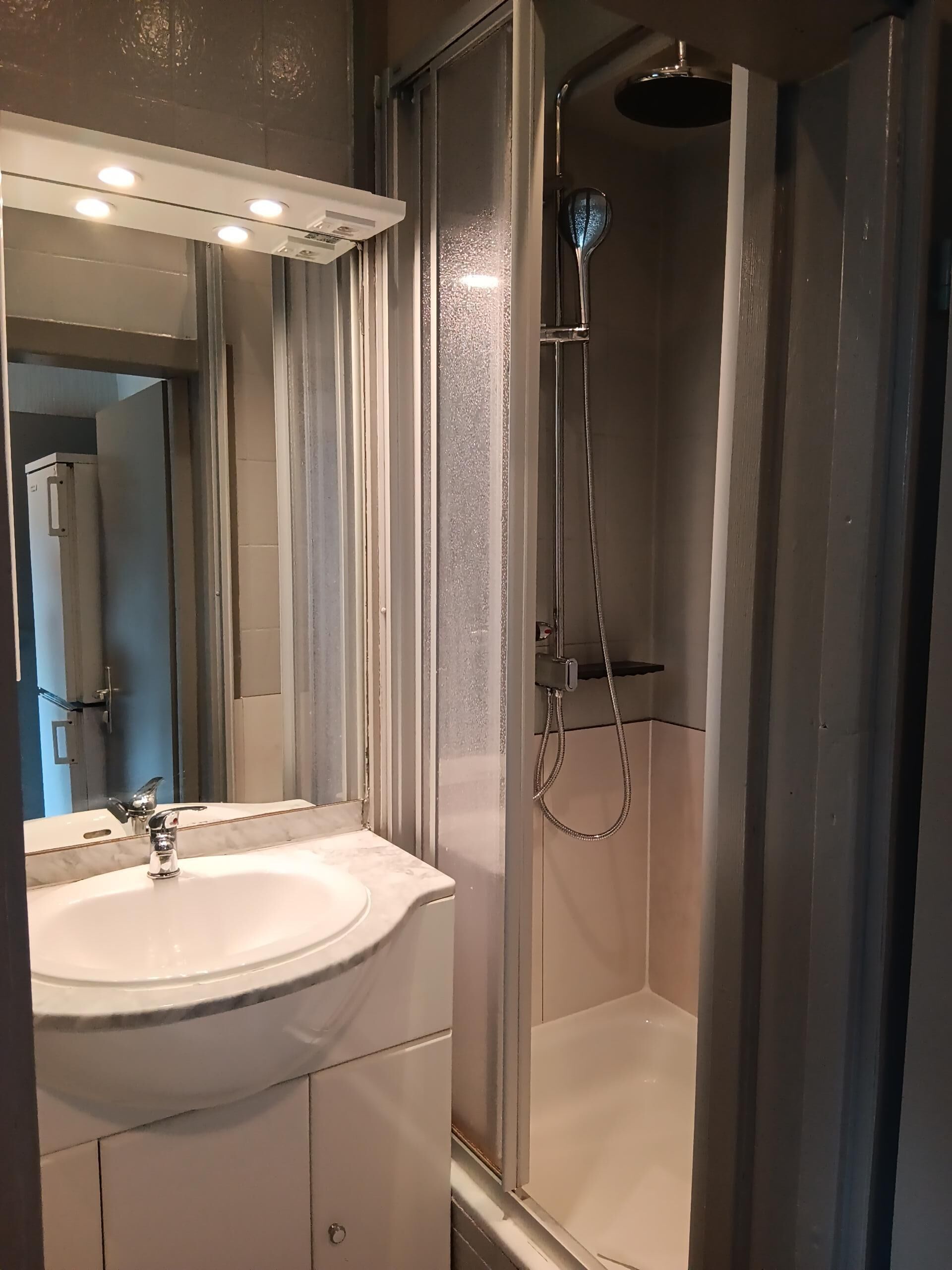 Un baño moderno con lavamanos blanco, espejo y cabina de ducha.