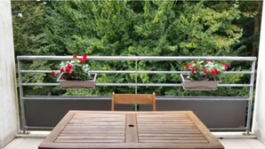 A balcony with a wooden table and two potted plants with red flowers. - Sudio + terrace 8m² center, beaches, south & parking (Anglet)