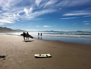 A beach with people walking and carrying surfboards.