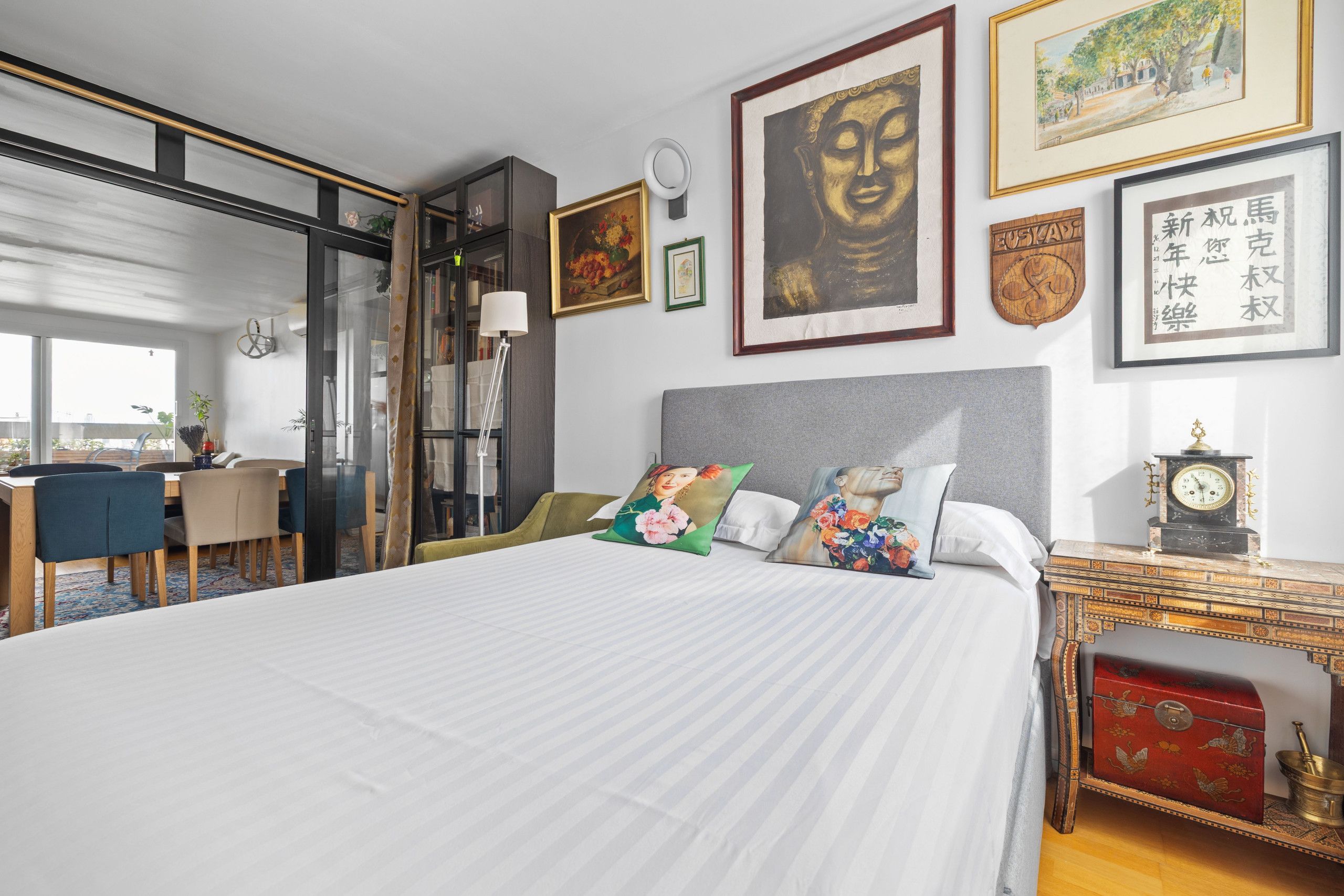 A hotel room with a large bed, a desk, and a chair. There are framed artworks on the wall and a clock on the nightstand.